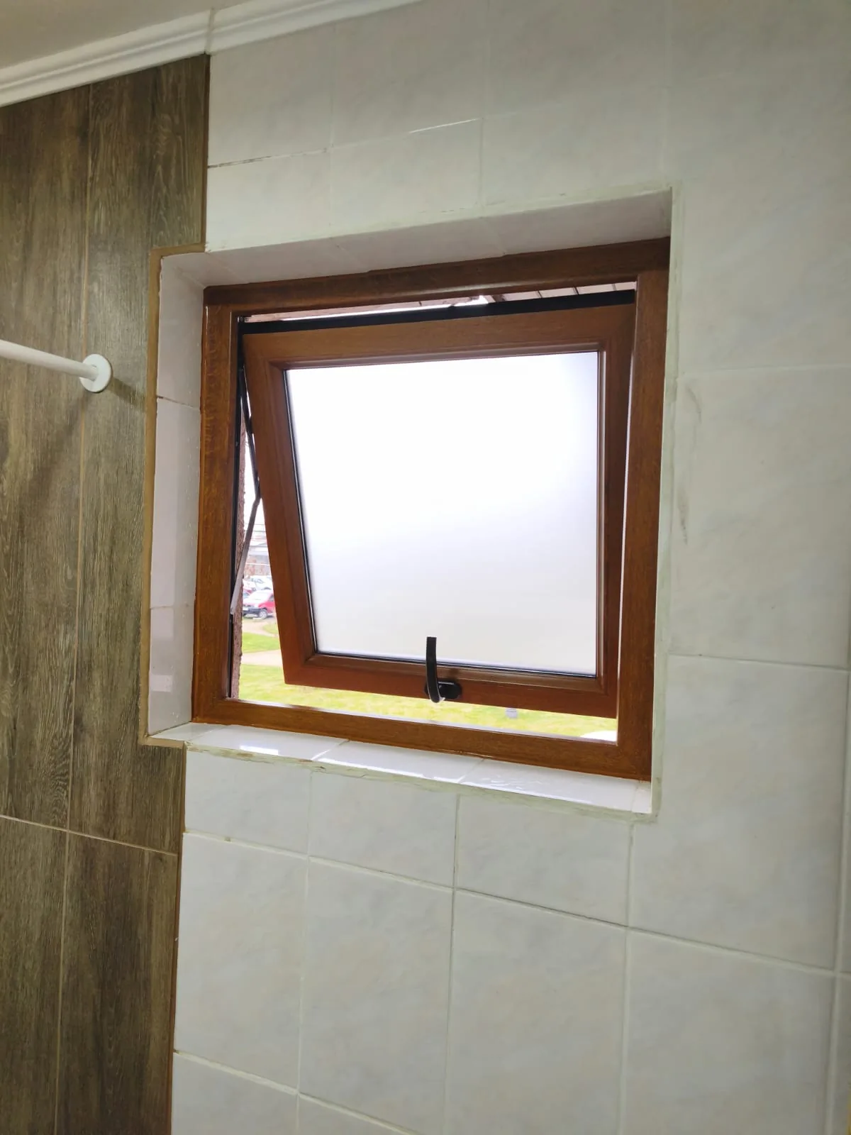 Ventana proyectante de PVC acabado madera con vidrio satinado instalada en baño